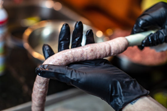 sausage fed into casings, held by palm next to stuffer horn