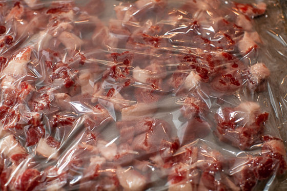 pork cubes spread on sheet pan covered with plastic wrap