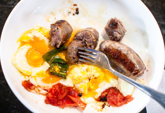 plate with half eaten sausages, eggs, chili, tomato and fork