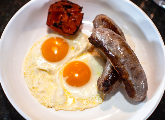 plate of two sunny-side eggs, grilled tomato and two English Banger sausages