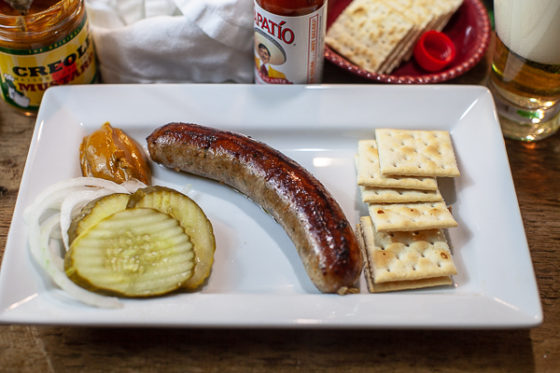 plate with boudin, crackers, creole mustard, pickles, onions, beer and hot sauce in background