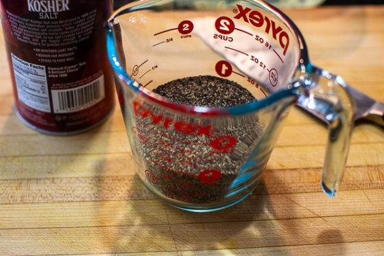 glass measuring cup containing pepper, salt container sitting on wooden cutting board