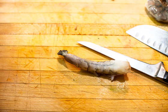 raw shrimp on its back on cutting board with knife
