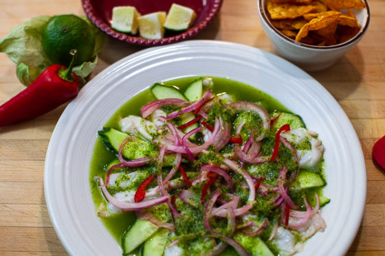Plated aguachile with cucumbers, pickeled onion and jalepeno garnished with chips and lime.