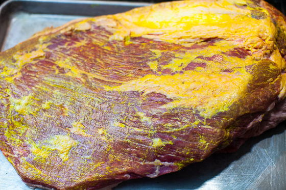 underside of uncooked brisket smoothered with layer of yellow mustard 