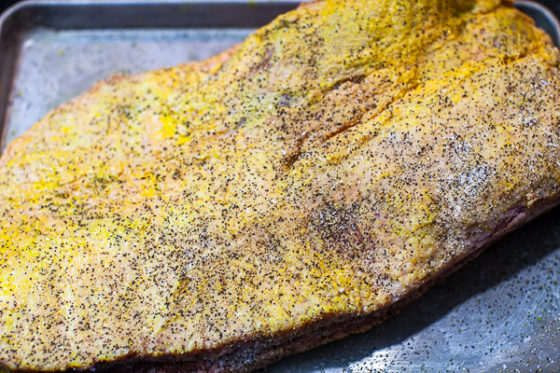 uncooked top of brisket slathered with mustard and sprinkled with salt and pepper