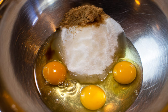 metal mixing bowl containing three eggs, salt, brown sugar and flour