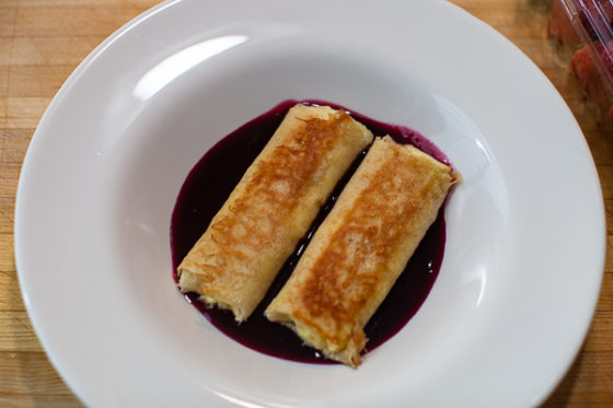 two cheese blintzes in center of cherry syrup in bowl