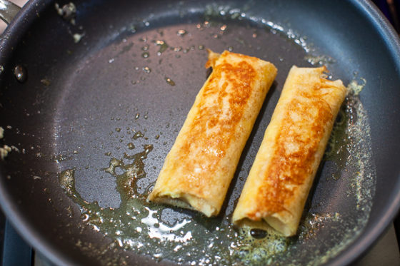 two browned crepes cooking in non-stick skillet