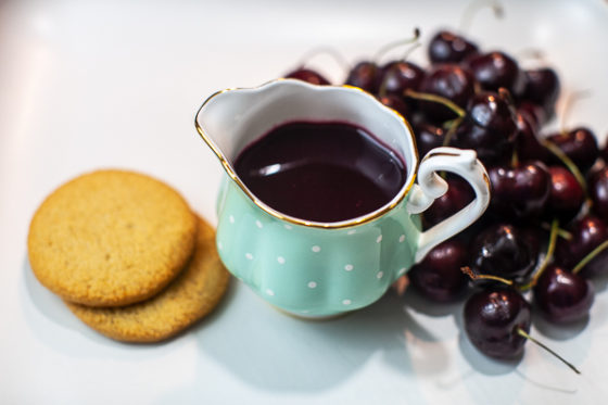 turquoise creamer containing cherry syrup next to cherries and shortbread cookies