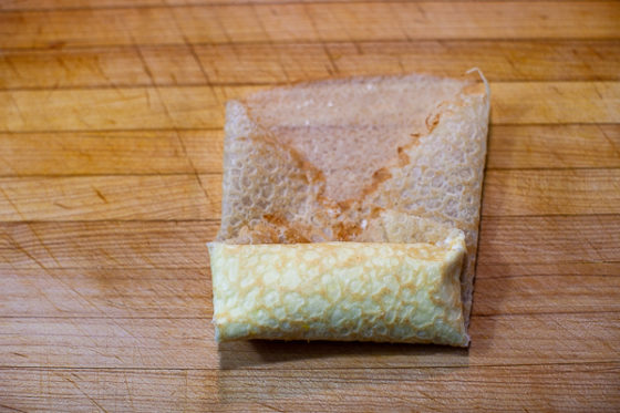 crepe being rolled on cutting board