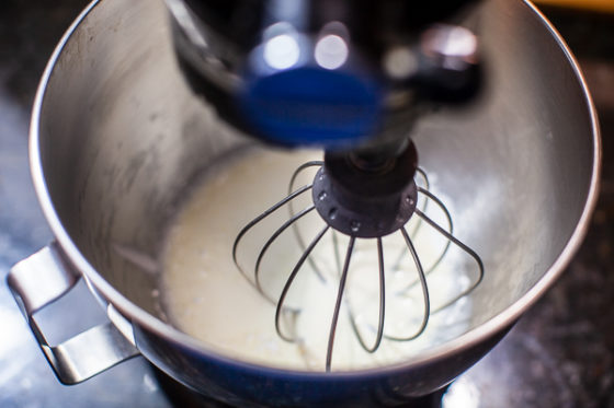 stand mixer bowl containing cream with whisk attachment