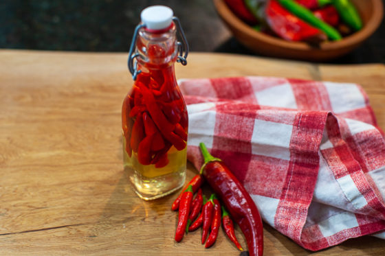 Small jar of pepper sauce next to fresh peppers on cutting board