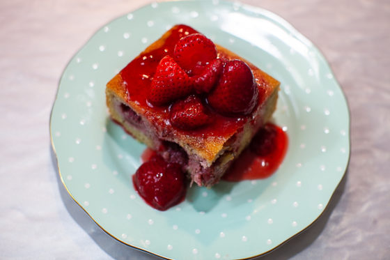 square of strawberry financier cake topped with strawberries and compote on plate
