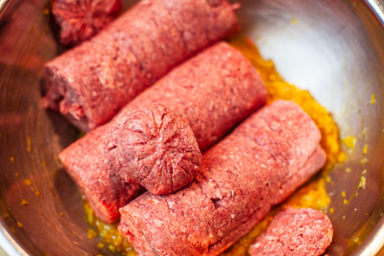 rolls of ground beef added to onion, turmeric, saffron water, salt and pepper mixture in bowl