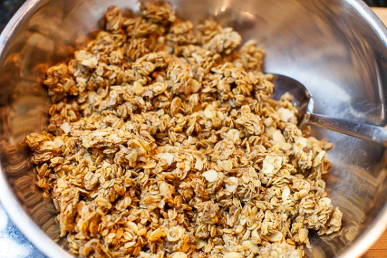 granola mixture in a metal mixing bowl, mixed with spoon
