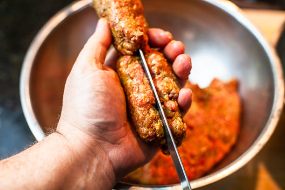 meat mixture being in palm of hand being pressed around flat metal skewer