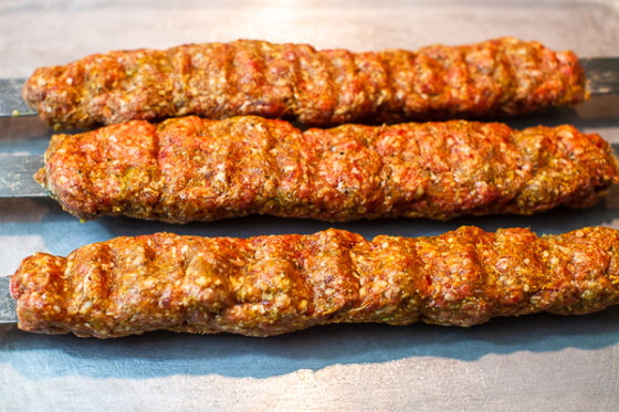 three kebabs (meat mixture around flat metal skewers) on cookie sheet
