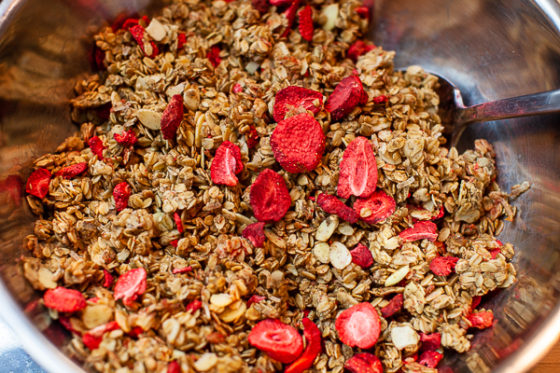 metal mixing bowl containing granola and dried strawberries, mixed with spoon