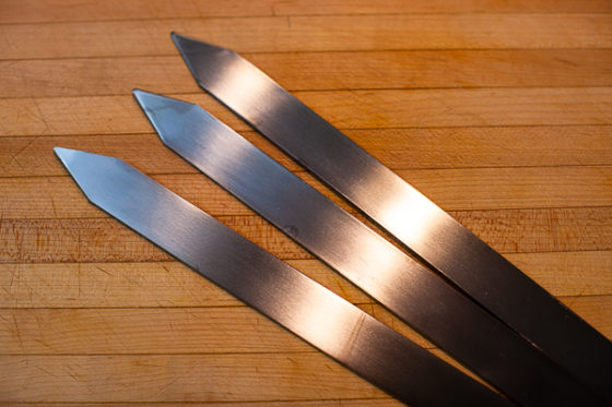 three large flat metal skewers on wooden cutting board