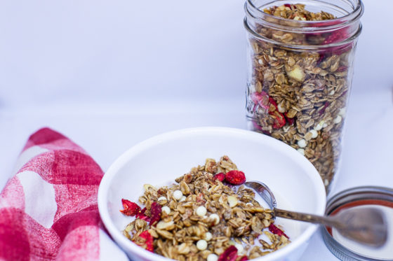 bowl containing granola and milk next to red and white checkered napkin and jar of granola