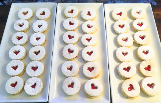 Three dozen Linzer cookies with heart shaped cut-outs on trays.