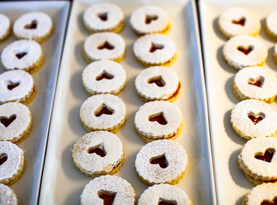 Plate of linzer cookies with heart shaped cutouts, powdered sugar and strawberry filling.