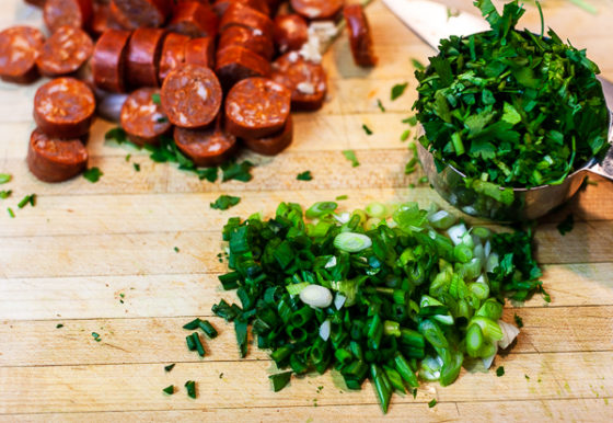 andouille sausage, cilantro, green onion (scallions) on wooden cutting board.