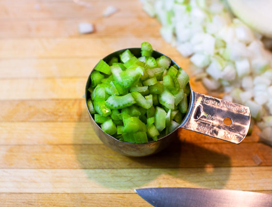 one cup measuring cup containing diced celery on cutting board. 
