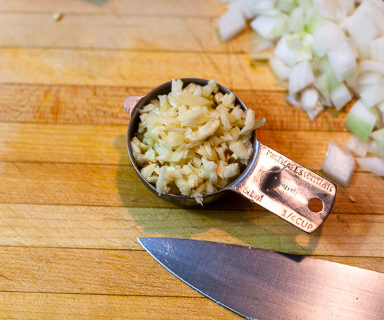1/4 cup of chopped garlic on a wooden cutting board.