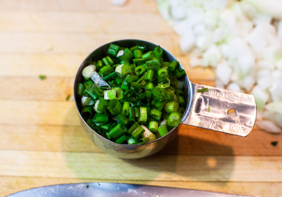 One measuring cup of diced scallions on wooden cutting board.