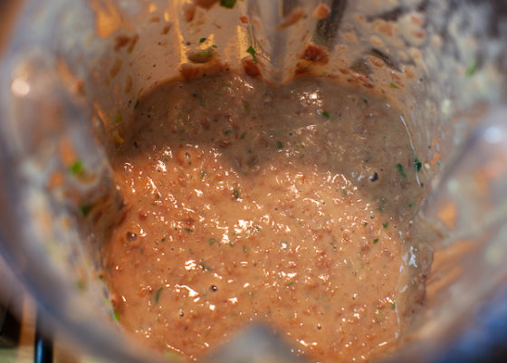 Blender containing purred beans, veggies, spices, ham, bacon and stock.