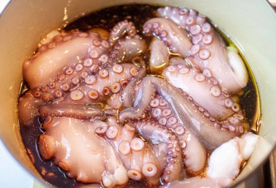 Trimmed and prepared Octopus in large pot with braising liquid.